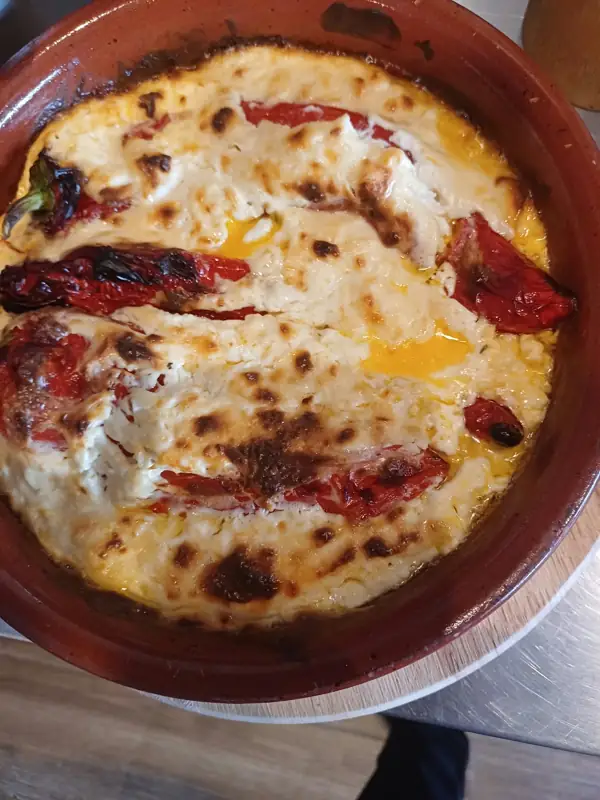Poivrons rouges cuits au four dans un plat en terre, sous du fromage gratiné